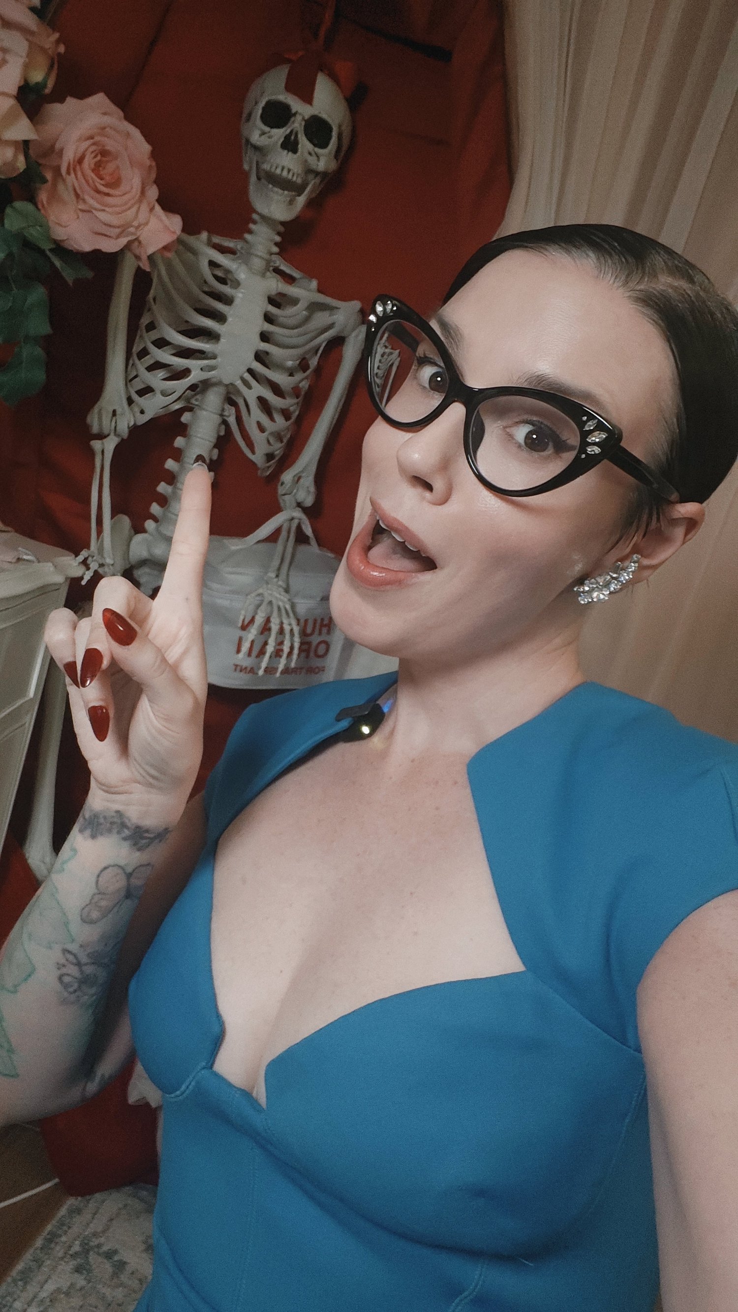 Sara in cat-eye glasses, posing with her skeleton friend